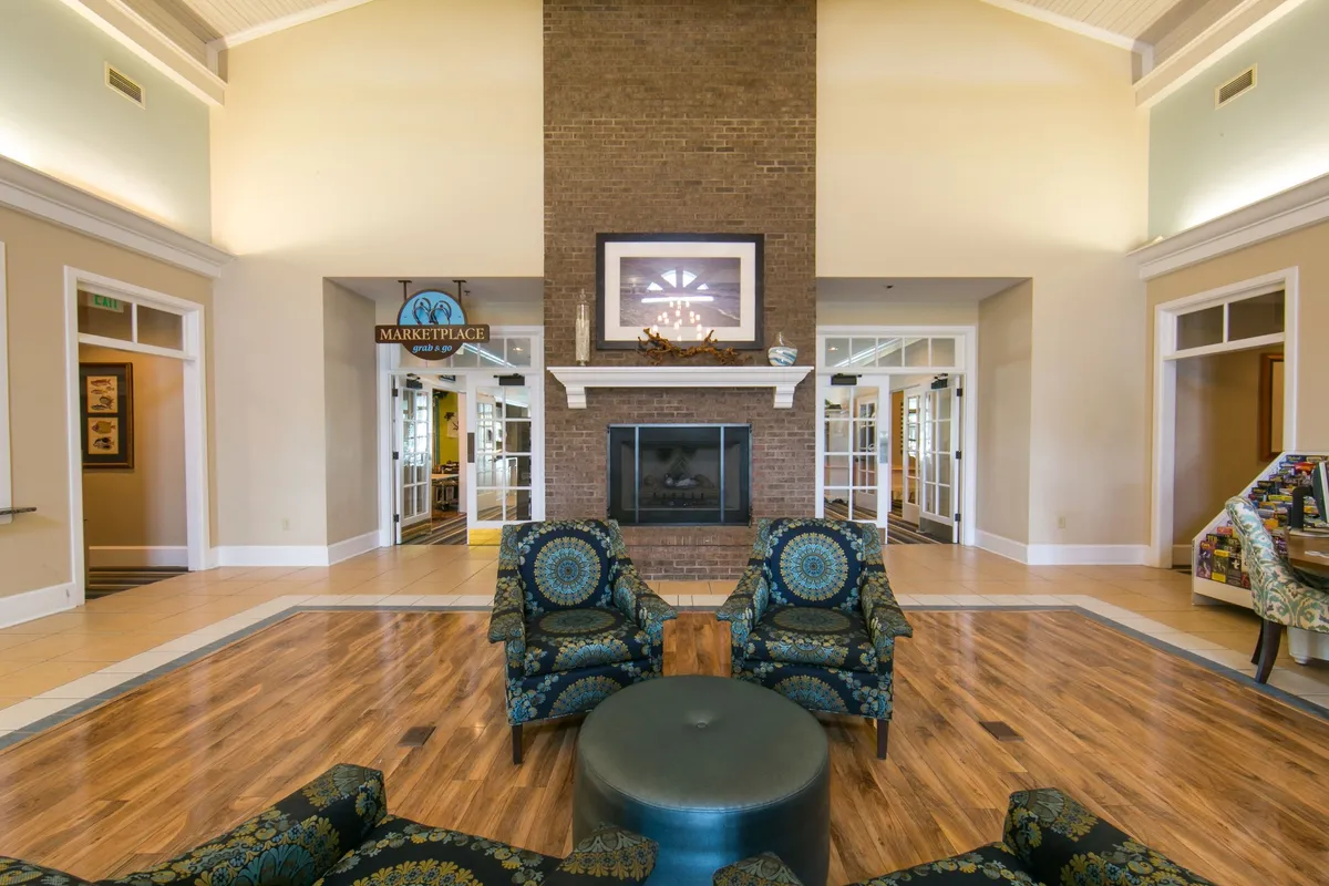 This interior image features a spacious lounge area with a large brick fireplace, blue patterned chairs, and a round coffee table. The 'Marketplace' sign indicates a social and communal atmosphere, ideal for relaxation and gathering before or after wellness activities.