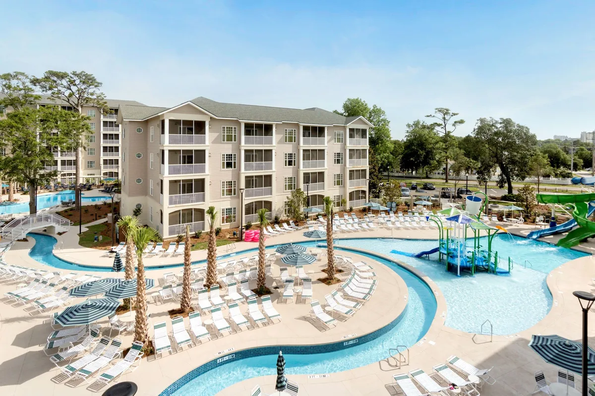 This lively exterior scene features a sparkling swimming pool, dramatic water slides, palm trees, and guests lounging under the sun. Children are spotted playing on the slides, while others swim or relax nearby, capturing the spirit of summertime aquatic fun.