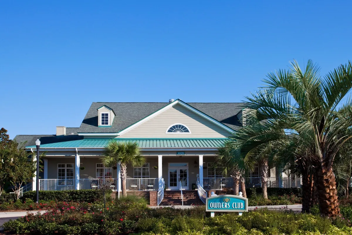 This image captures the inviting exterior of the clubhouse, featuring elegant signage and lush, well-maintained landscaping. The scene radiates a welcoming and serene atmosphere, ideal for couples seeking a tranquil escape. The clubhouse hints at the amenities available within, such as the indoor pool, hot tub, and sauna, while suggesting a vibrant community backdrop for romantic getaways.
