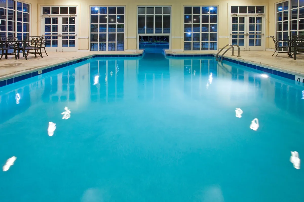 A serene interior view of the spacious indoor swimming pool, featuring large windows that let in natural light and a calm seating area with chairs. The tranquil setting conveys year-round accessibility and a relaxing escape, perfect for unwinding after active play.