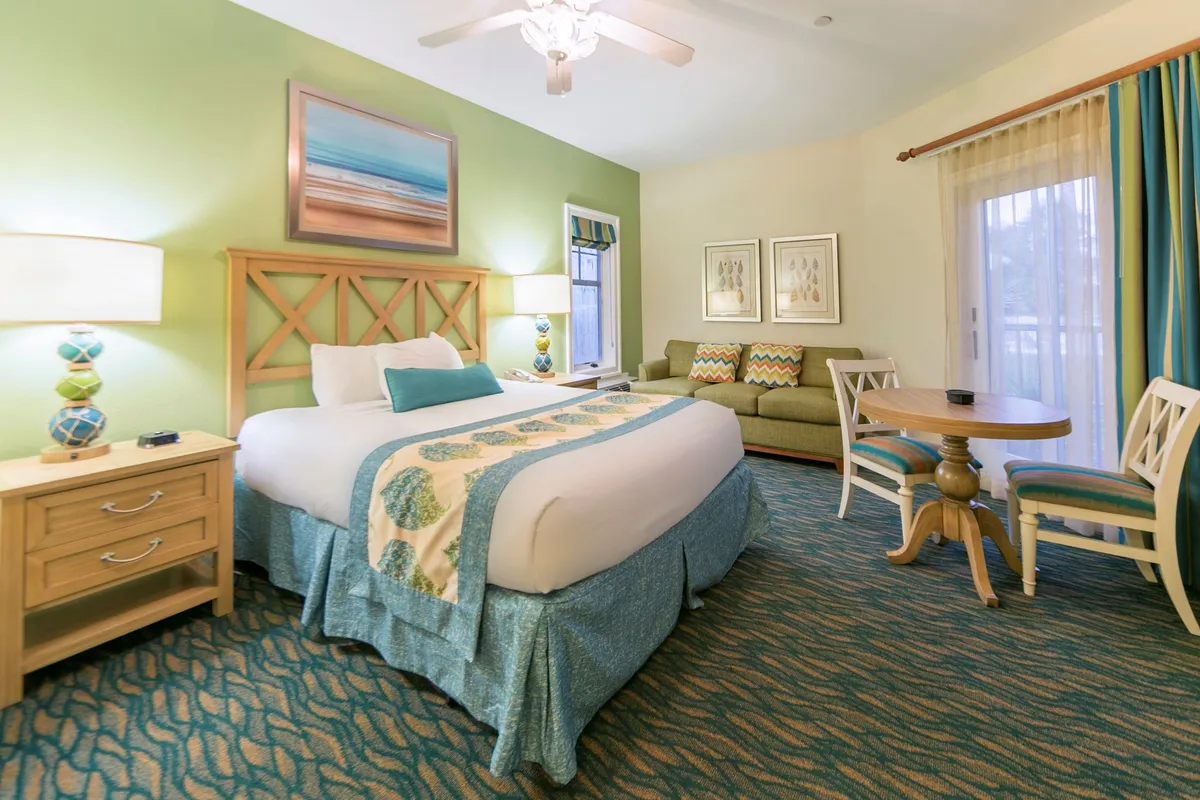 A close-up interior view focusing on a bed adorned with a decorative quilt, a green sofa for lounging, and a round dining table positioned for shared meals or quiet mornings. The scene is bathed in natural light, creating an inviting and vibrant ambiance ideal for relaxing, reading, or enjoying a cup of coffee.